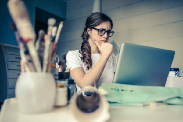 A woman rests her chin on her hand and appears distressed as she reads from her laptop.