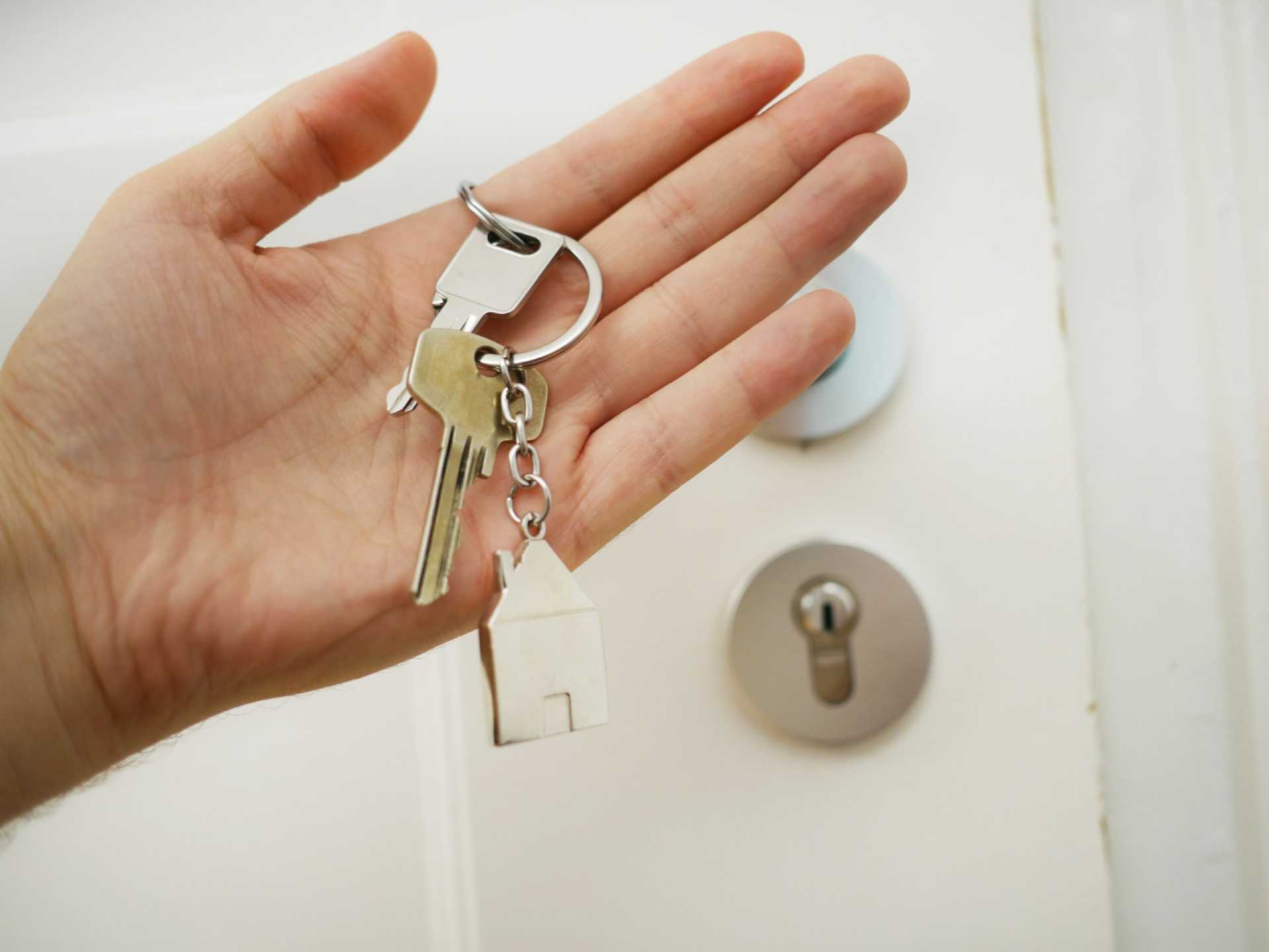 A hand holding house keys next to a locked front door.