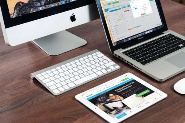 A range of devices on a desk, including a computer, laptop and tablet.