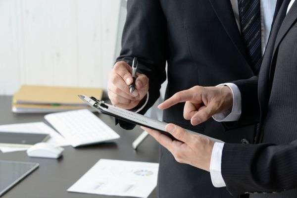 Two male business partners discuss and annotate a document on a clipboard.