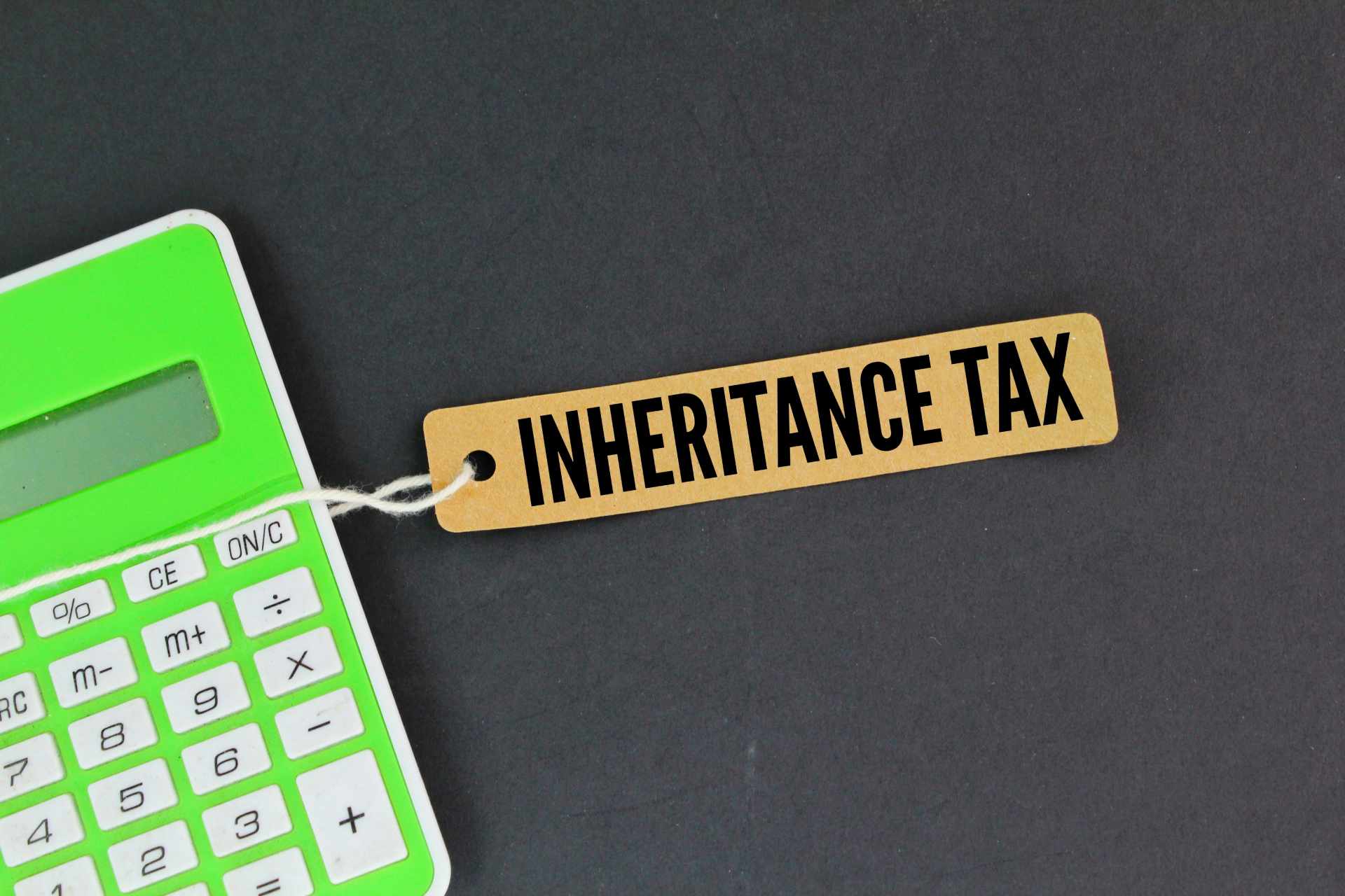 a green calculator with a tag saying inheritance tax attached to it on a grey background