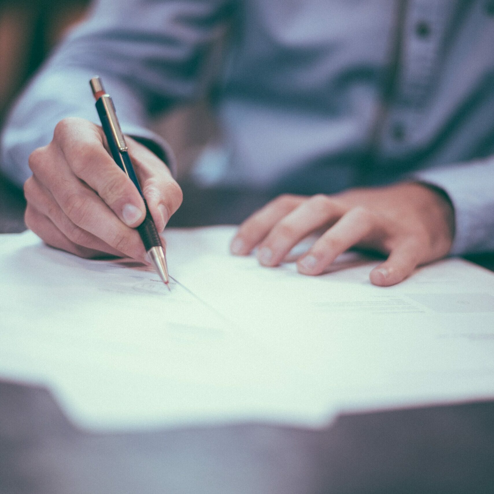 A closeup of a male signing documents whilst sat at a table.